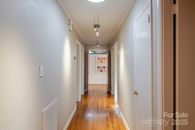 corridor featuring light wood-style floors, baseboards, ornamental molding, and visible vents