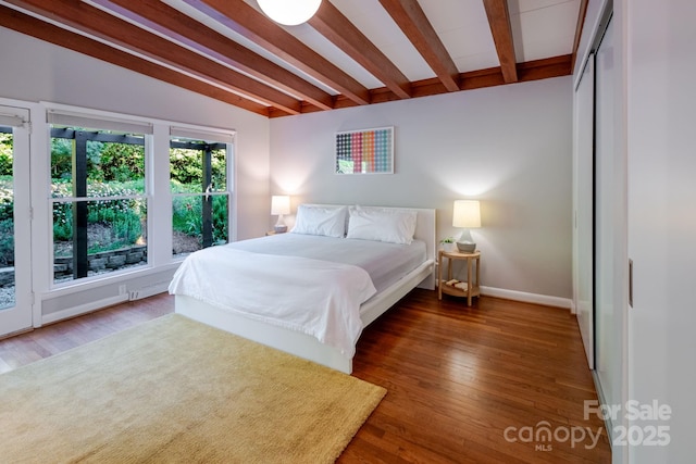 bedroom with baseboards, lofted ceiling with beams, and wood finished floors
