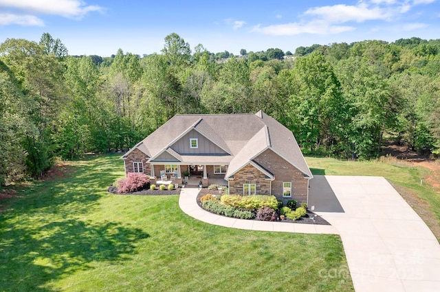 craftsman-style home featuring a wooded view, concrete driveway, a porch, and a front yard