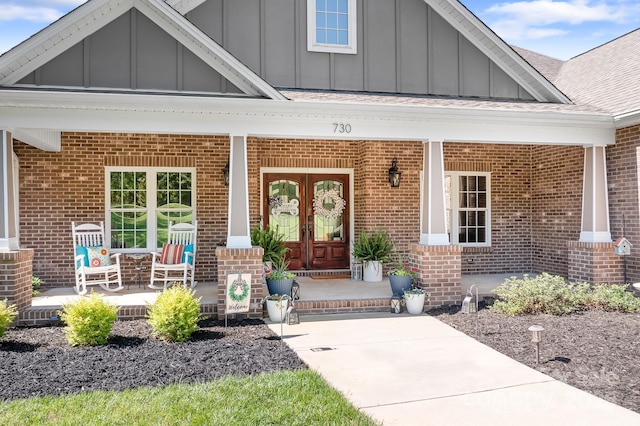 doorway to property with board and batten siding, a porch, and brick siding