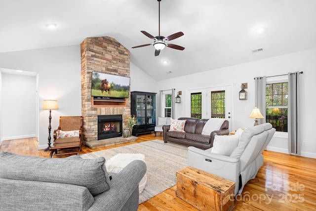 living room featuring light wood finished floors, high vaulted ceiling, a stone fireplace, a ceiling fan, and baseboards