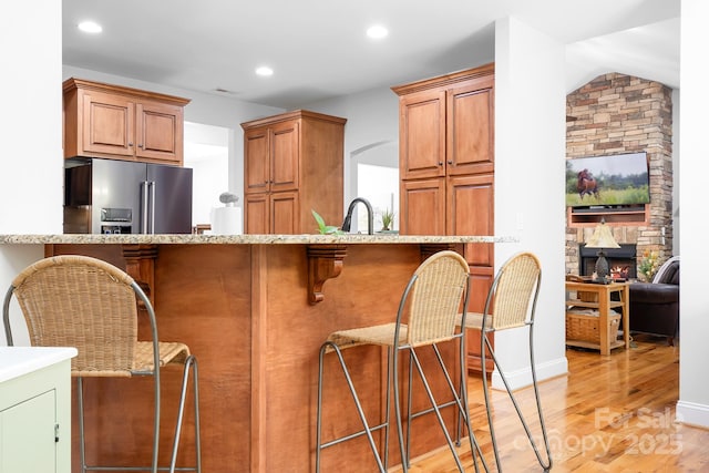 kitchen featuring a kitchen bar, high quality fridge, light stone counters, light wood finished floors, and recessed lighting