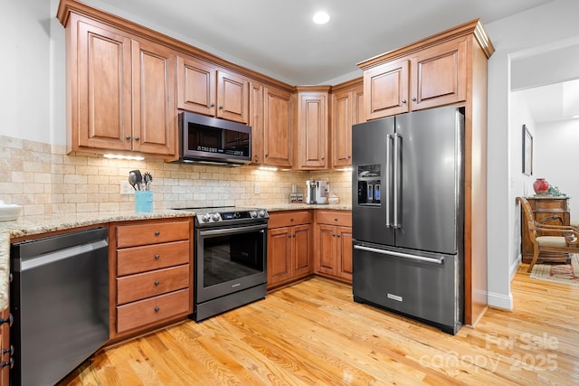 kitchen with light wood-type flooring, backsplash, light stone countertops, and stainless steel appliances