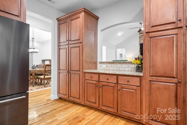 kitchen with light wood-type flooring, freestanding refrigerator, ceiling fan, and brown cabinets