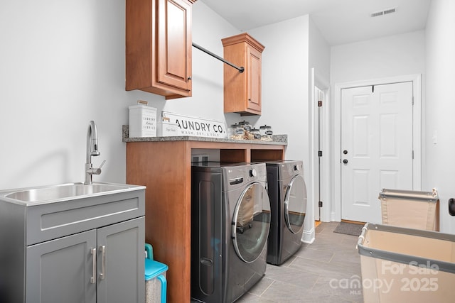 washroom with cabinet space, visible vents, washing machine and dryer, and a sink