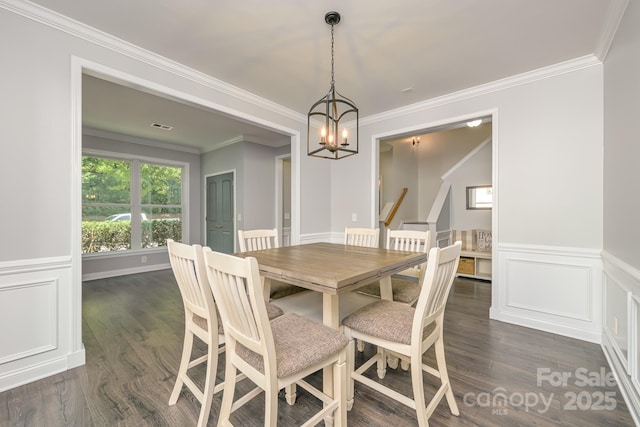 dining room with a chandelier, dark wood-type flooring, ornamental molding, and a wainscoted wall