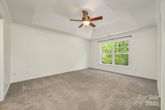 empty room featuring a raised ceiling, a ceiling fan, carpet, baseboards, and crown molding