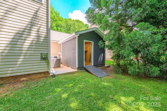 back of property with a lawn, a storage shed, an outbuilding, central AC, and roof with shingles