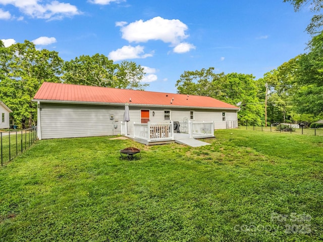 rear view of house with a wooden deck, a fenced backyard, a yard, a fire pit, and metal roof