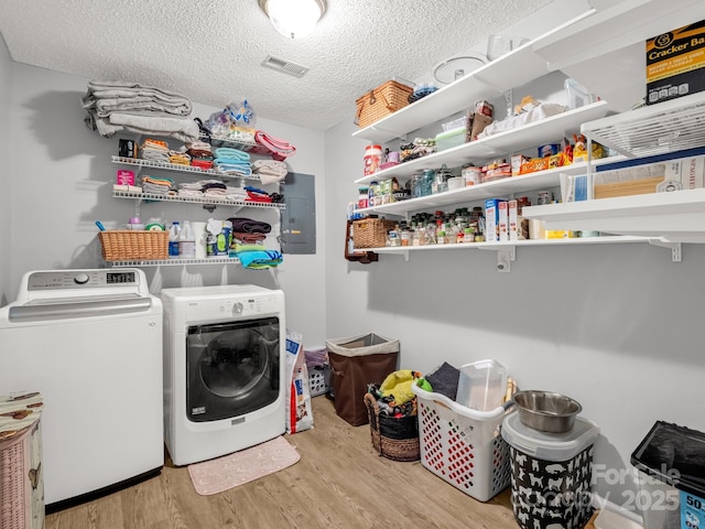 clothes washing area with laundry area, a textured ceiling, wood finished floors, visible vents, and washing machine and dryer