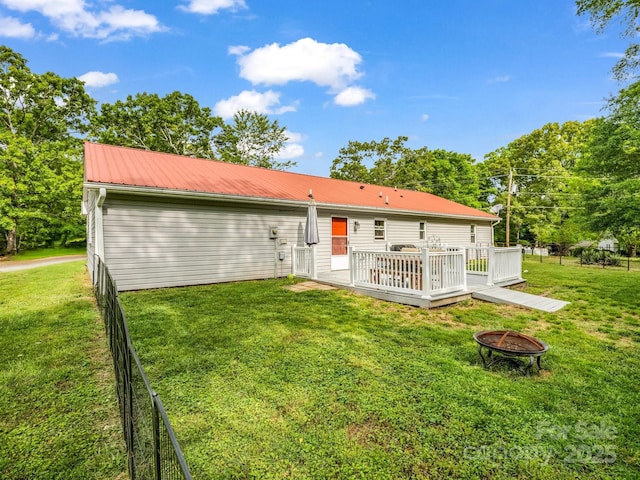 back of house with metal roof, a wooden deck, fence, a yard, and a fire pit