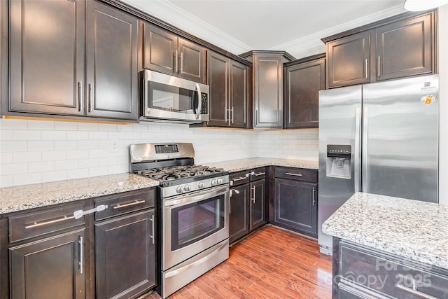 kitchen featuring dark brown cabinets, light stone counters, ornamental molding, stainless steel appliances, and light wood-style flooring