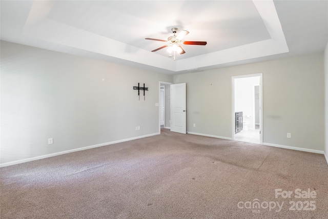 carpeted spare room featuring baseboards, a raised ceiling, and ceiling fan