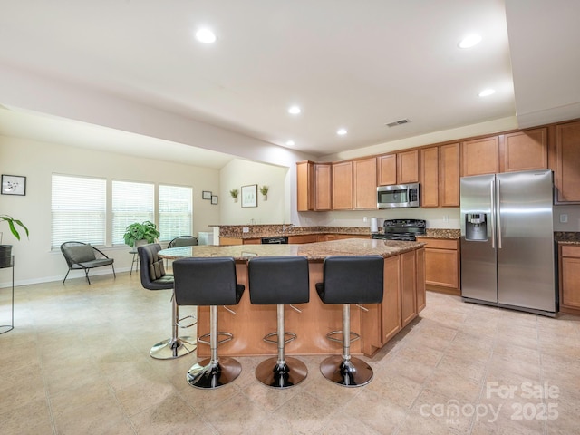 kitchen with light stone countertops, recessed lighting, brown cabinetry, a kitchen bar, and stainless steel appliances