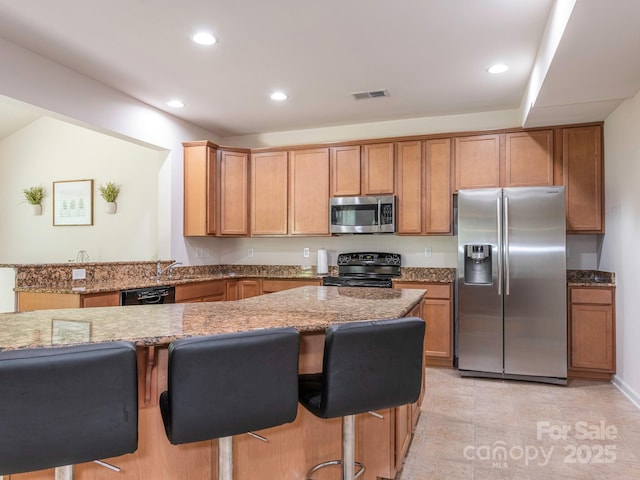 kitchen featuring a breakfast bar, a sink, black appliances, light stone counters, and recessed lighting