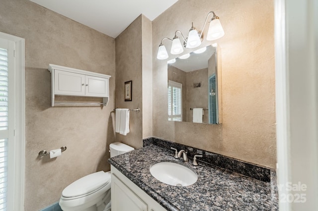 bathroom featuring toilet, vanity, and a textured wall