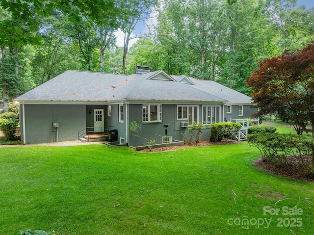 rear view of property featuring a lawn, a chimney, central AC unit, and a shingled roof