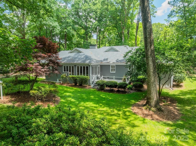 rear view of property with a lawn, a chimney, a deck, and roof with shingles