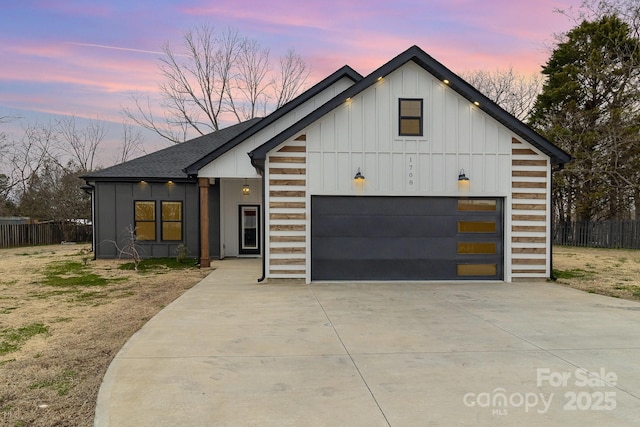view of front of property featuring a garage, driveway, board and batten siding, roof with shingles, and fence