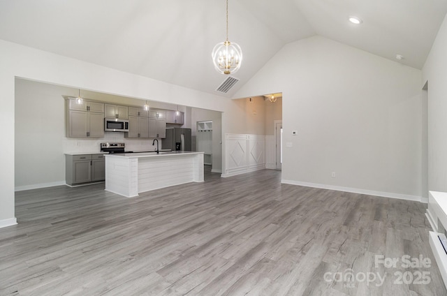 unfurnished living room featuring a sink, an inviting chandelier, light wood-style floors, high vaulted ceiling, and visible vents