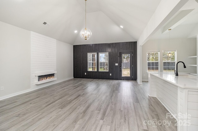 unfurnished living room with a large fireplace, an inviting chandelier, light wood-type flooring, wooden walls, and visible vents