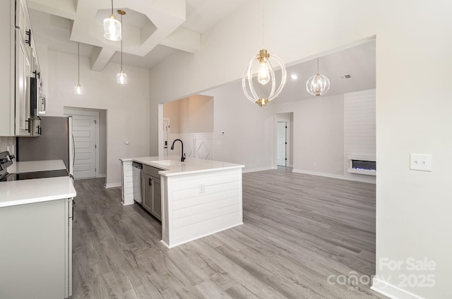 kitchen with a sink, coffered ceiling, light wood-type flooring, a towering ceiling, and a center island with sink