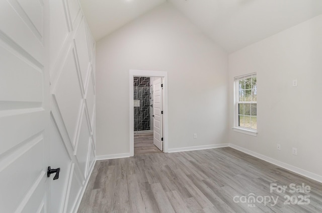 unfurnished bedroom featuring high vaulted ceiling, baseboards, a spacious closet, and light wood-type flooring