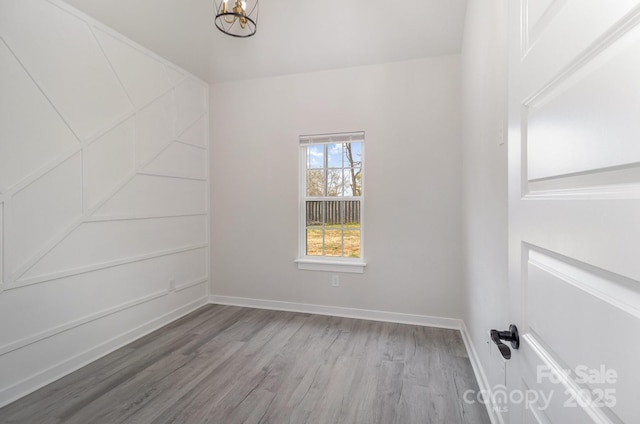 unfurnished room with an inviting chandelier, wood finished floors, and baseboards