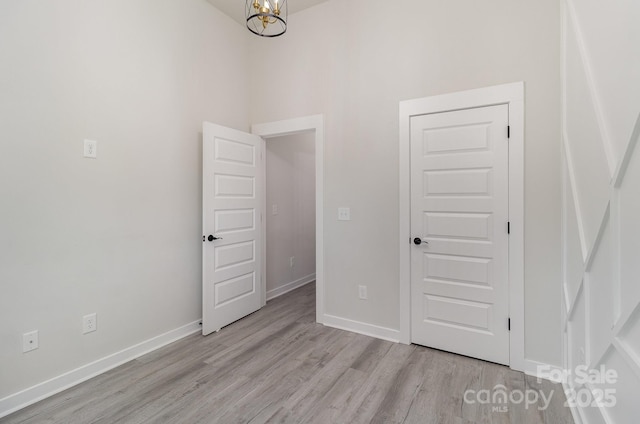 unfurnished bedroom featuring a chandelier, baseboards, and light wood-style floors