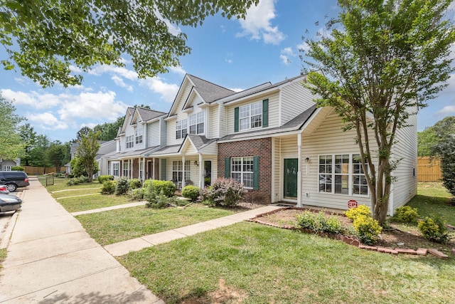 view of front of house featuring brick siding, fence, a front yard, and roof with shingles
