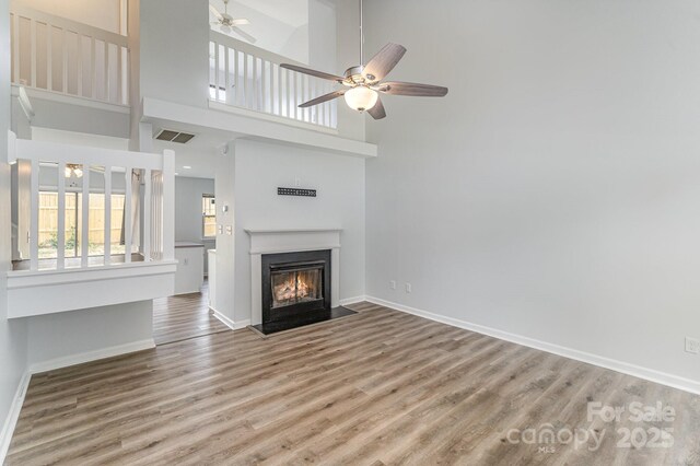 unfurnished living room with visible vents, wood finished floors, baseboards, ceiling fan, and a fireplace with flush hearth