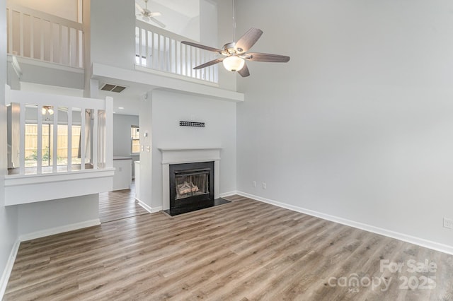 unfurnished living room featuring visible vents, a fireplace with flush hearth, wood finished floors, baseboards, and a ceiling fan