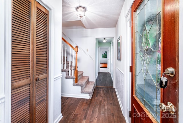 corridor with stairs, a textured ceiling, baseboards, and dark wood-type flooring