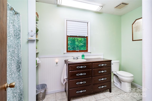 bathroom with wainscoting, tile patterned flooring, vanity, toilet, and visible vents