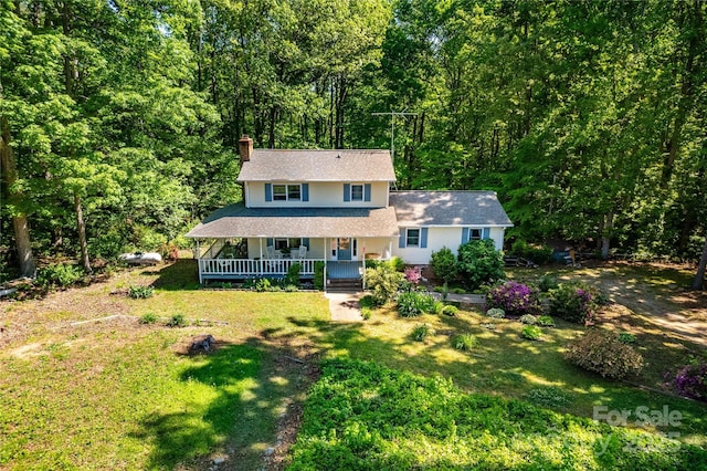 view of front of home featuring a view of trees, a front yard, covered porch, and a chimney