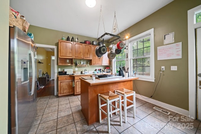 kitchen featuring a breakfast bar, a kitchen island, light countertops, visible vents, and stainless steel refrigerator with ice dispenser