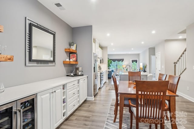 dining room with light wood-style floors, recessed lighting, wine cooler, visible vents, and stairway