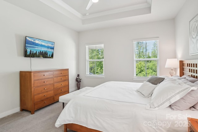 bedroom featuring ceiling fan, light colored carpet, multiple windows, and a raised ceiling