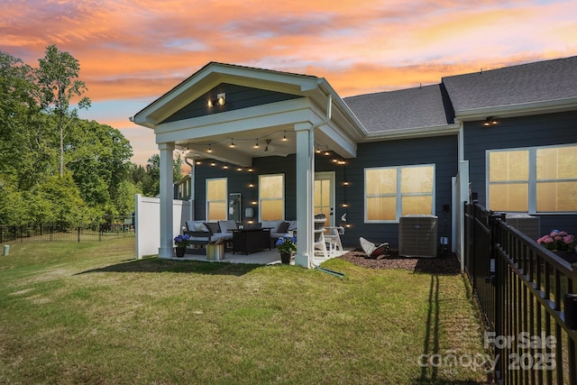 back of property at dusk featuring a lawn, a patio area, central air condition unit, fence, and outdoor lounge area