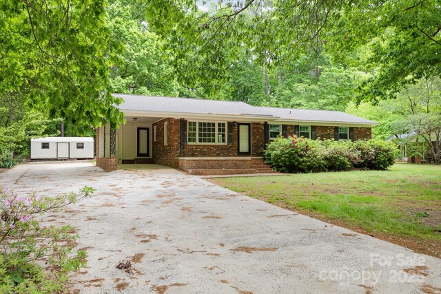ranch-style home with brick siding, driveway, an outbuilding, and a front yard