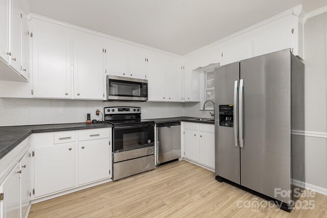 kitchen featuring dark countertops, appliances with stainless steel finishes, a sink, light wood-style floors, and backsplash