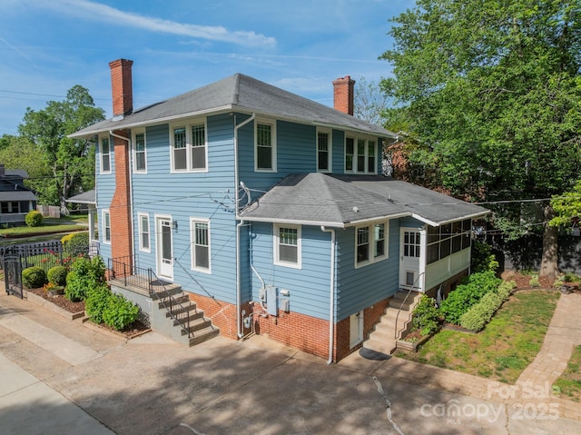 view of front facade featuring a shingled roof, a chimney, a sunroom, and driveway