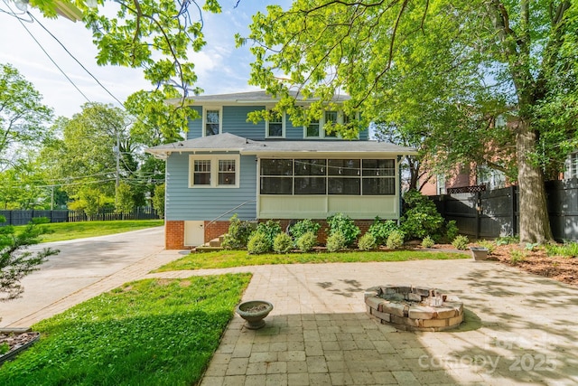back of house featuring a patio area, a fire pit, fence, and a sunroom