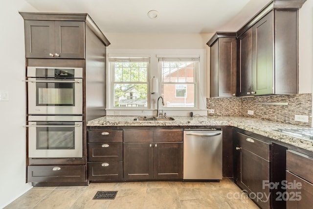 kitchen with a sink, dark brown cabinetry, stainless steel appliances, and light stone countertops