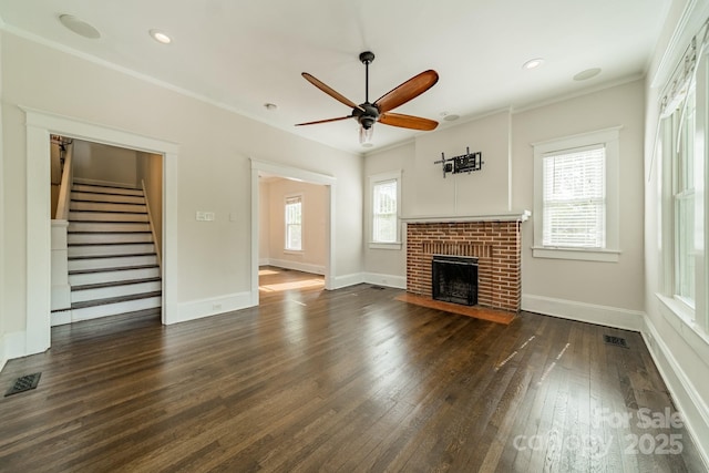 unfurnished living room featuring ornamental molding, stairs, a fireplace, ceiling fan, and dark wood-type flooring