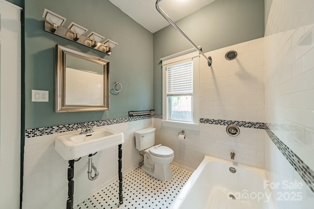 bathroom with tile walls, wainscoting, a sink, toilet, and washtub / shower combination