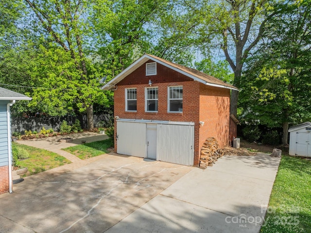 garage featuring a storage unit, fence, and concrete driveway