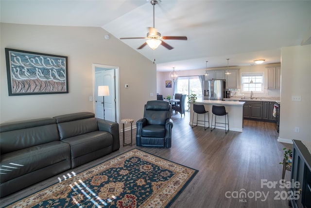 living area with ceiling fan with notable chandelier, vaulted ceiling, and dark wood finished floors