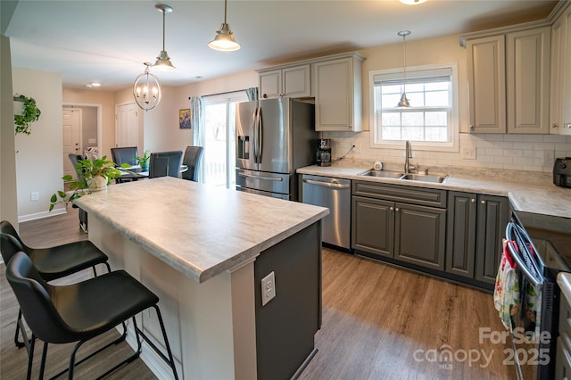kitchen featuring a sink, light wood-style floors, a kitchen breakfast bar, tasteful backsplash, and appliances with stainless steel finishes