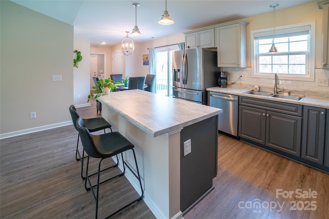 kitchen featuring a kitchen breakfast bar, a sink, stainless steel appliances, dark wood-type flooring, and gray cabinets